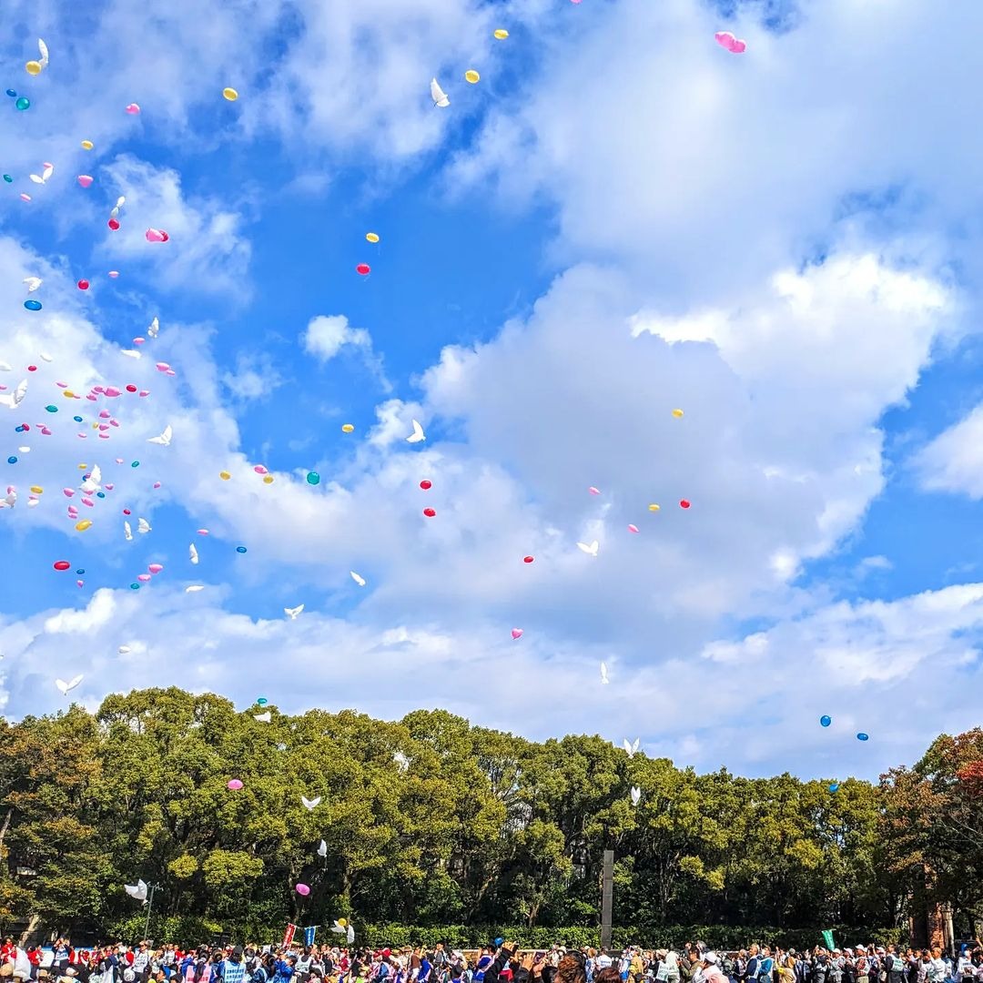 「平和の想いをのせて」 青空のもと集まった人々がバルーンリリースをしている写真