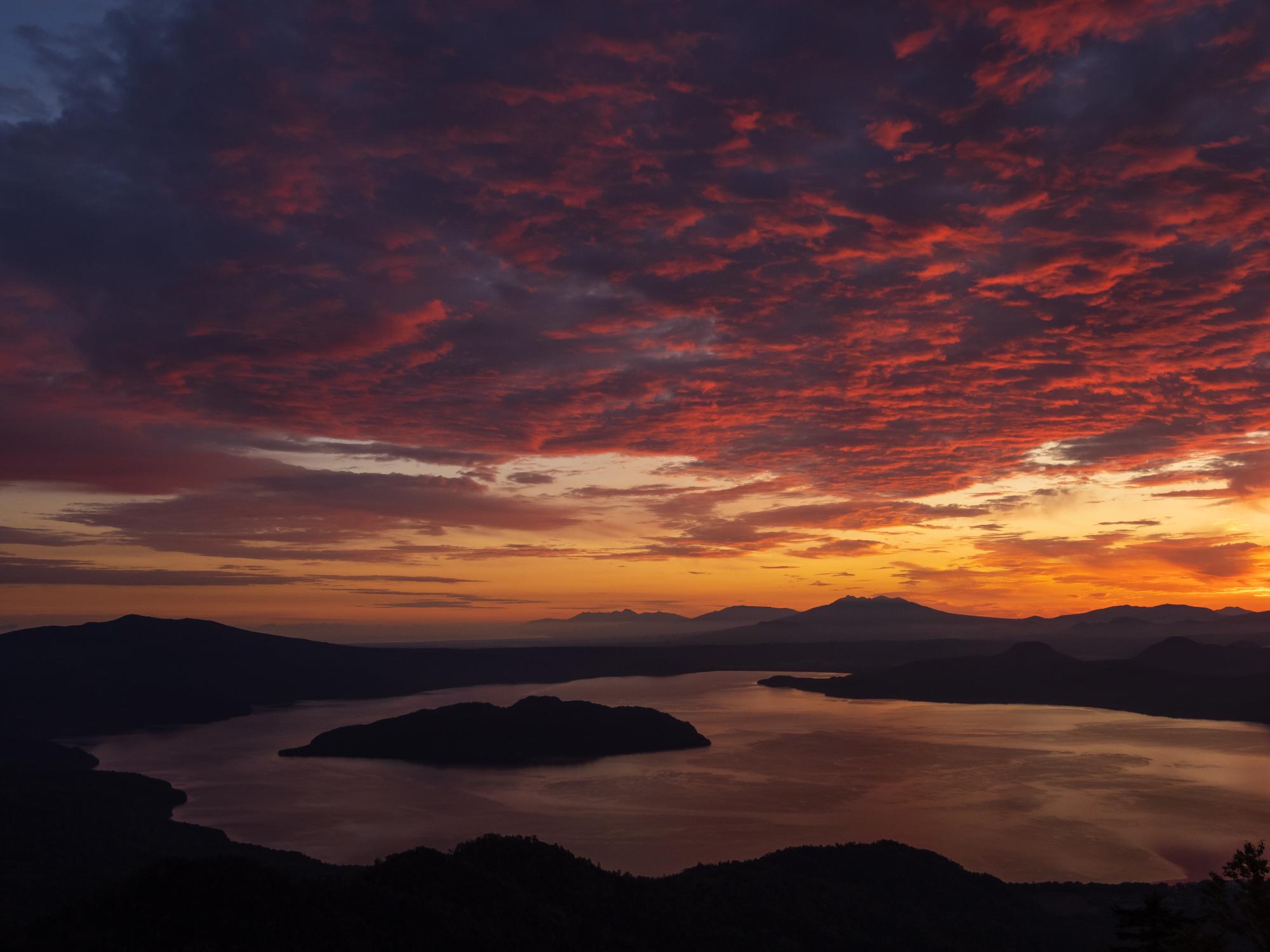 朝焼けに染められた赤い雲とそれを映す湖面を捉えた写真