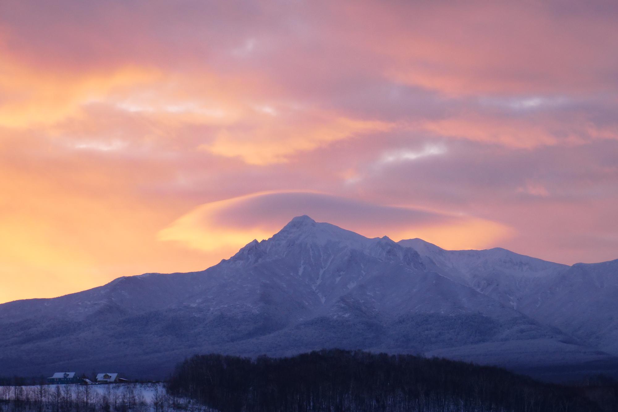 山の上にかかっている帽子雲が朝焼けに照らされている様子を捉えた写真