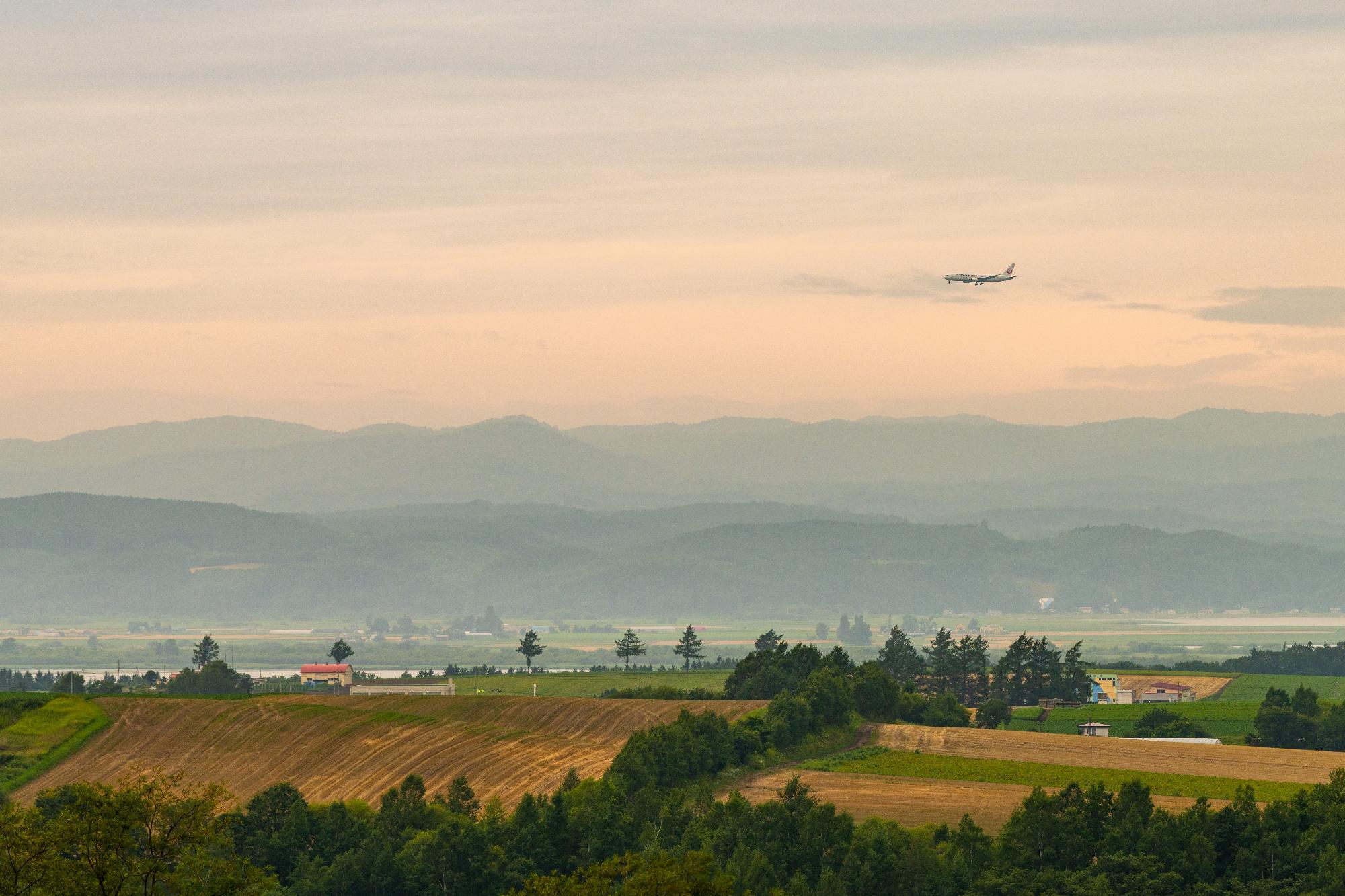 田園風景が広がる地上と空を飛んでいる飛行機を捉えた写真