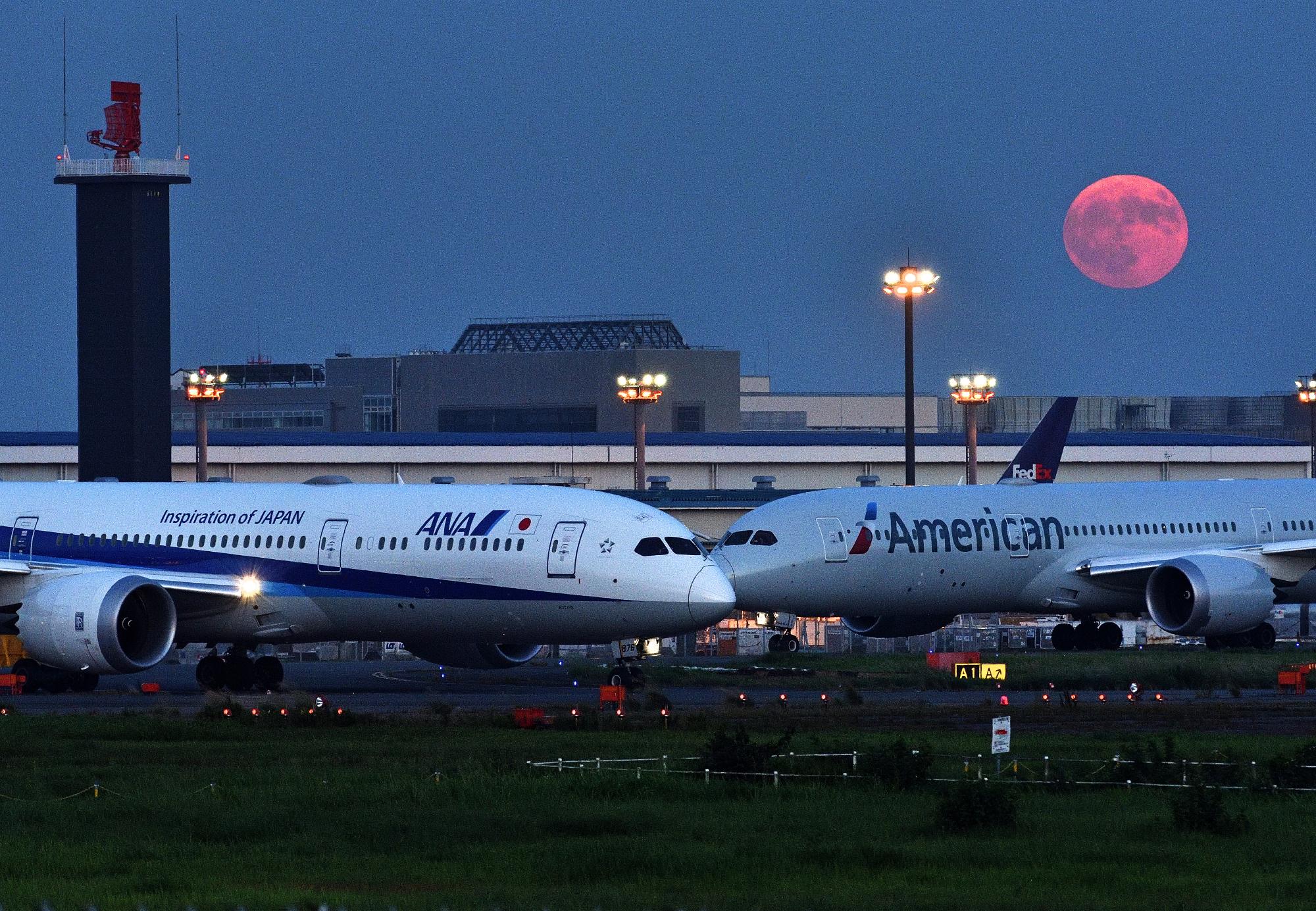 飛行機が2体並んでいる上空を赤い月が照らしている様子を捉えた写真