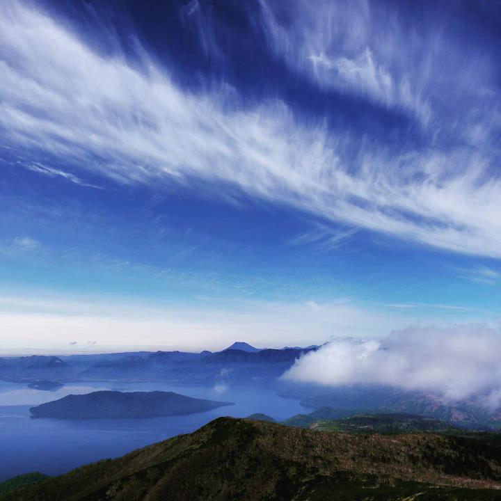 湖の上空で濃淡のある青い空に雲がかかっている様子を捉えた写真