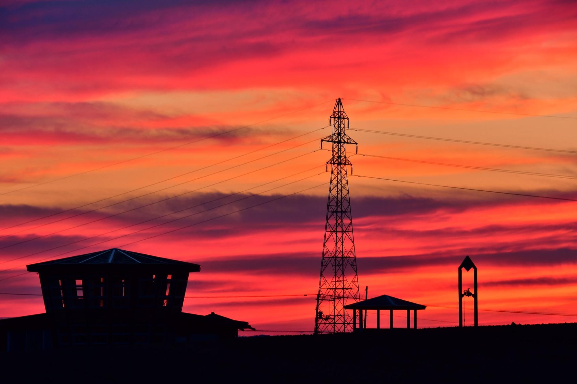 赤々とした雲と送電塔や建物がシルエットになっている状態を捉えた写真