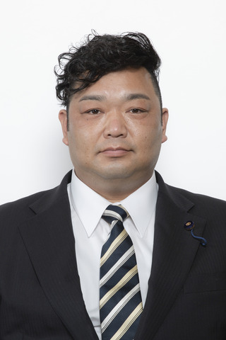 黒いスーツに紺、黄色、シルバーのストライプのネクタイをしめた大泉知功さんが正面を向いている写真