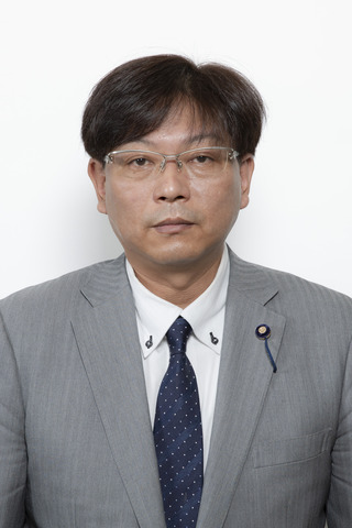 ライトグレーのスーツに紺色の水玉のネクタイをしめてめがねをかけている川村淳さんが正面を向いている写真