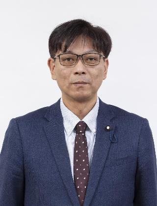 紺色のスーツにエンジ色の水玉のネクタイをしめてメガネをかけている川村淳さんが正面を向いている写真