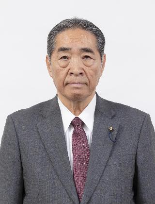 グレーのスーツにエンジ色のネクタイをしめた松岡克美さんが正面を向いている写真