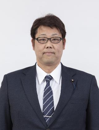 黒いスーツにストライプのネクタイをしめてメガネをかけた仲西政克さんが正面を向いている写真