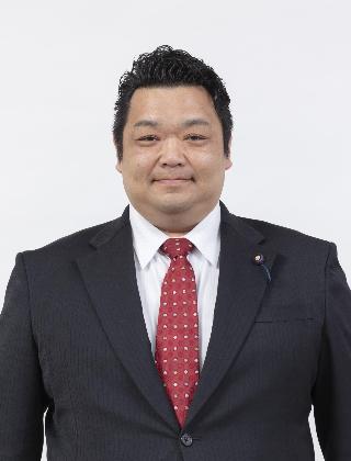 黒いスーツに赤の水玉のネクタイをしめた大泉知功さんが正面を向いている写真
