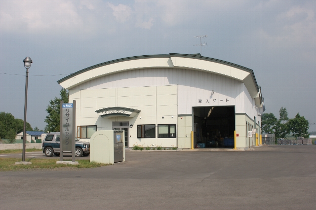 アーチ型の屋根にアイボリー色の外壁で正面入り口の右横に広く開いた受け入れゲートがある建物の写真