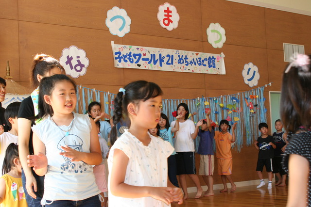 壁に「なつまつり」と貼られた広い室内でたくさんの子どもたちが並んで踊っている様子の写真