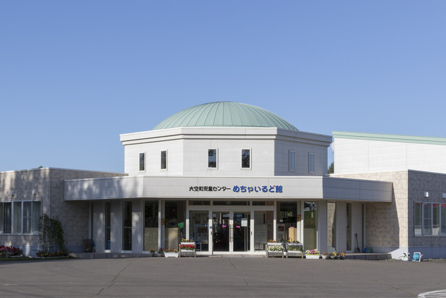 ミントグリーン色の丸い屋根が特徴的な建物の入口に花のプランターが置かれているめちゃいるど館の写真