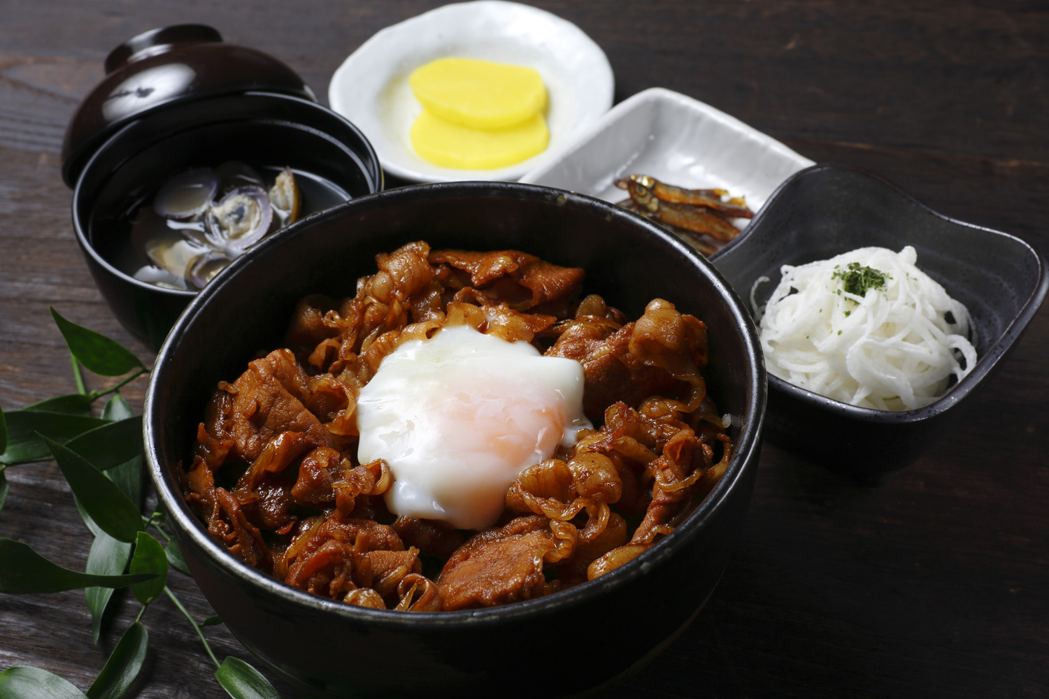 ごはんの上に豚肉を煮たものと半熟卵がのったどんぶり、お吸い物、小魚と漬け物2種の3つの小皿がついた定食の写真