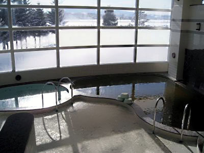 格子状の大きな窓から外の雪景色が臨める広い浴室の写真
