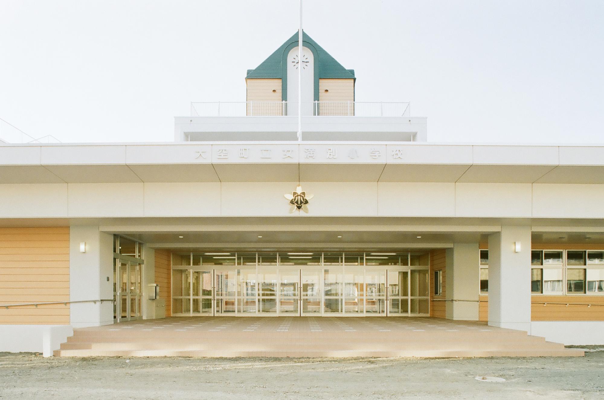 広い正面玄関中央に校章が飾られ、上の階には緑色の三角屋根の時計台がある校舎の写真