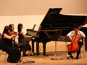 グランドピアノ、ヴァイオリン、チェロをそれぞれ演奏する男女4名の写真