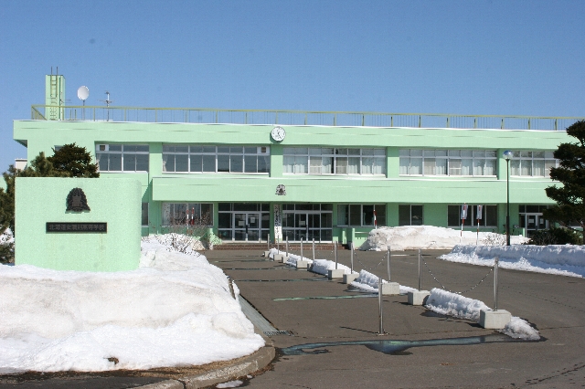 青空の下雪の残った門と奥に建つ緑色の校舎の写真