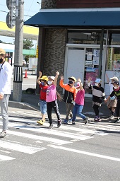 2人1組で手をつなぎながら手を上げて横断歩道を歩いている小学生たちの写真その1