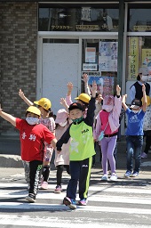 2人1組で手をつなぎながら手を上げて横断歩道を歩いている小学生たちの写真その2