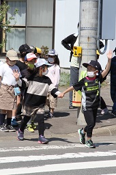 2人1組で手をつなぎながら手を上げて横断歩道を歩いている小学生たちの写真その3