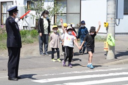 警察官と先生に見守られながら2人1組で手をつなぎながら手を上げて横断歩道を歩いている小学生たちの写真