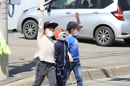 3人1組で手を上げて道路を横断している小学生の写真