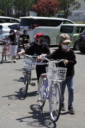駐車場で一列になって自転車を手押しして移動している小学生たちの写真