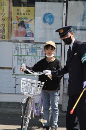 自転車のハンドルを持って立っている女子小学生とそれを静止している警察官の写真