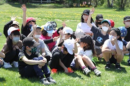 芝生に座りながら手を上げている小学生たちの写真