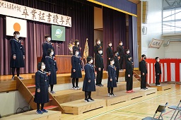 壇上のひな壇に並んで合唱をしている卒業生たちの写真