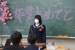 黒板に卒業おめでとうと描かれている前で話をしている女子中学生の写真