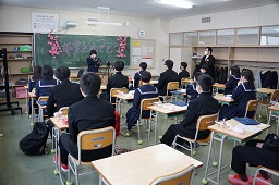 卒業する女子中学生の話を椅子に座って聞いている卒業生たちの写真