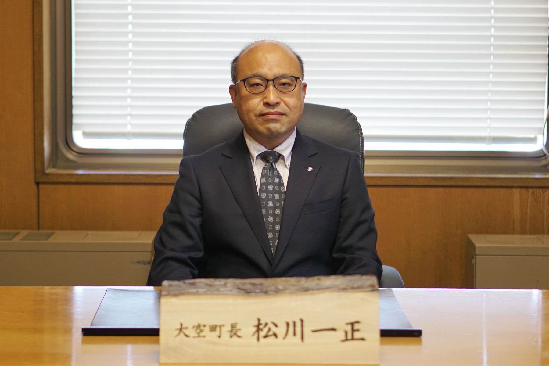 大空町長 松川一正と書かれた札が置かれた机に座る町長の写真