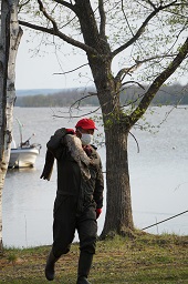 湖畔で枯木をかついでいる赤い帽子の参加者の写真