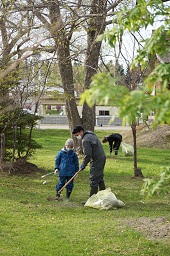 芝生で棒を持った男性とトングを持った男の子がゴミを探している様子の写真