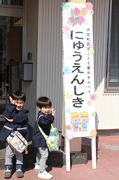 にゅうえんしきと書かれた立て看板の前でカバンを掛けながらポーズを取っている2人の男児の写真