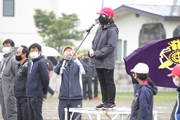 台に上がりマイクに向かって開会宣言をしている赤い帽子をかぶった女子小学生の写真