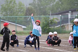 紅白の帽子をかぶった小学生たちが走る準備をしている中手を上げている赤い帽子をかぶった女の子の写真