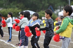 横一列になって赤いボンボンを持って踊っている小学生たちの写真