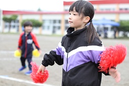 赤いボンボンを持って踊っている女子小学生の様子の写真