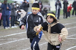 リレー競走で黄色いはちまきをしている男子小学生から女子小学生へバトンが渡された瞬間の写真