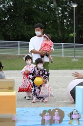 黄色いボールをピンに向かって転がそうとしている浴衣姿の女の子とそれを見ている浴衣姿の女の子と子どもを抱っこしている男性の写真