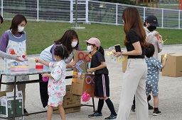 箱の中からくじを引いている女の子と引いたくじをスタッフに渡そうとしている女の子とそれを見守っている先生の写真