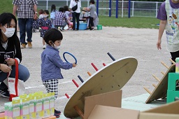 輪投げコーナーで青い輪っかを投げようとしている男の子と母親の写真