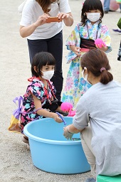 水風船を釣り上げようとしている浴衣姿の女の子とそれを見ているスタッフの写真