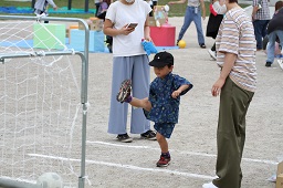 足を高々とシュートした男の子とゴールにボールが転がっている様子の写真