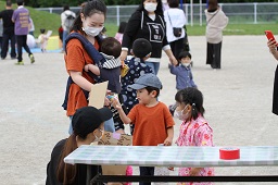 景品をもらった男の子と渡している赤ちゃんを抱っこしているお母さんとそれを見ている女の子とスタッフの写真