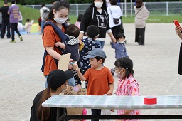 景品をもらった男の子と渡している赤ちゃんを抱っこしているお母さんとそれを見ている女の子とスタッフの写真