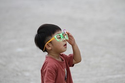 緑色のおもちゃのメガネをかけているワインレッド色のシャツを着た男の子の写真
