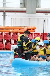 プールに浮いているボートに乗っているスタッフと6人の子どもたちの写真